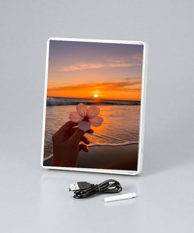 Digital photo frame displaying a sunset and hand holding a flower, with USB cable and stylus on a gray background.