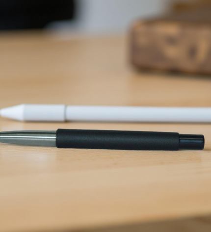 Two pens on a wooden surface, one black and silver, one white.