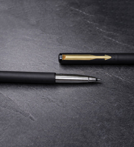 Two pens, one black and one with a gold clip, on a dark gray textured surface.