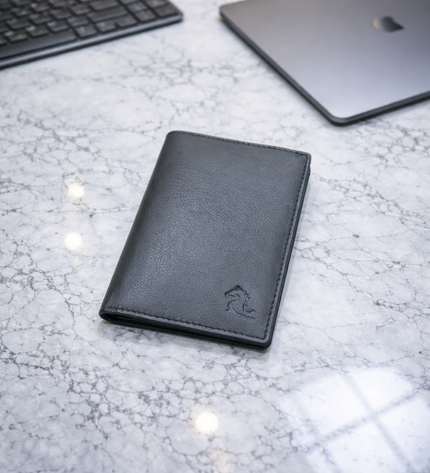 Black leather wallet on a marble surface with a laptop and keyboard in the background