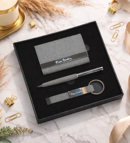 Business card holder, pen, and keychain set in a black box on a marble surface with decorative elements.