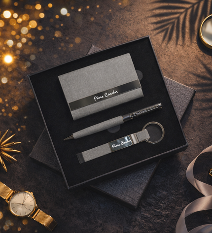 Pierre Cardin business card holder, pen, and keychain set in a black box on a dark surface with decorative elements.
