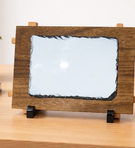 Wooden frame with a white slate on a wooden desk with a plant and cup in the background