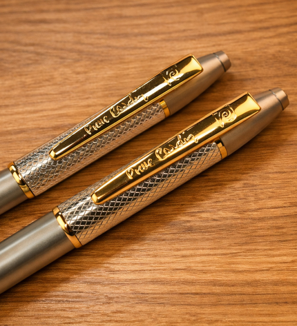 Two metallic pens with gold accents on a wooden surface