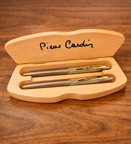 Three pens in a wooden box with 'Pierre Cardin' branding on a wooden surface