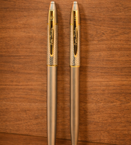 Two gold pens on a wooden surface