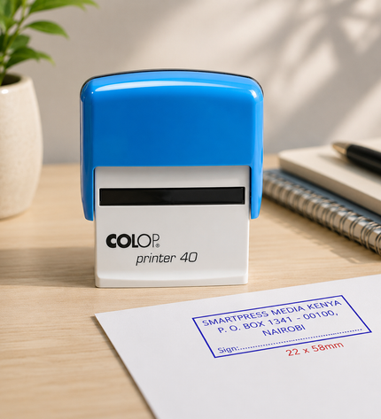 Colop printer 40 stamp on a desk with a plant and notebook in the background