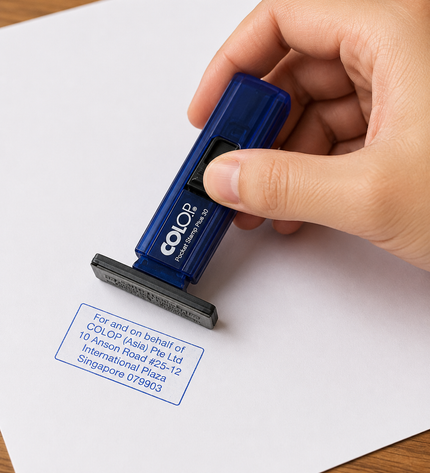 Hand using a Colop stamp on a piece of paper