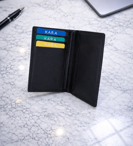 Black wallet with colorful cards on a marble surface with a keyboard and laptop in the background.