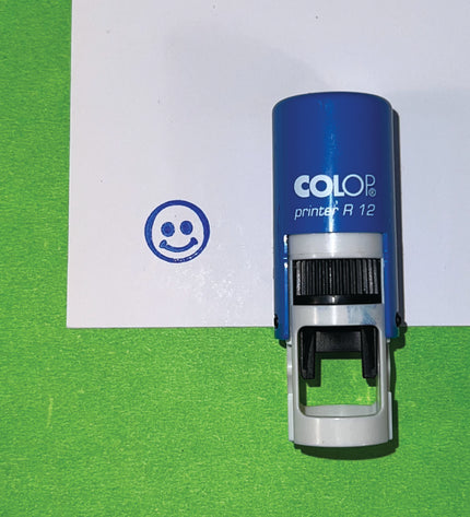 Colop printer A 12 stamp on a green and white background with a smiley face stamp impression.
