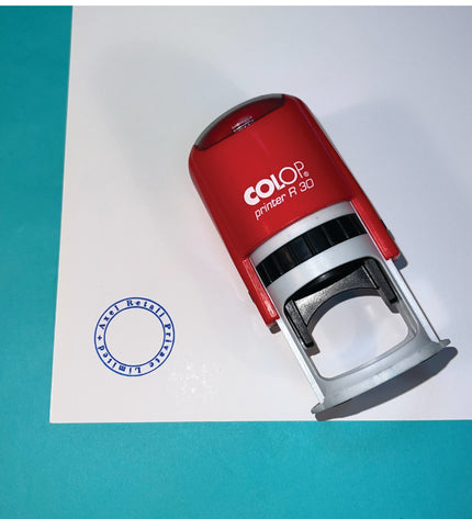 Red Colop printer on a white sheet of paper with a blue stamp impression.