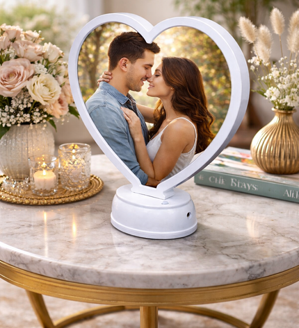 Heart-shaped photo frame with a couple's reflection on a marble table with decorative items.