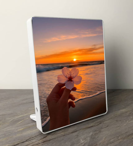 Tablet with a sunset and beach design on the screen, held by a hand holding a pink flower.