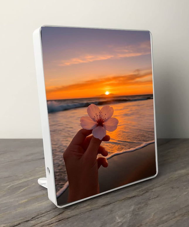 Tablet with a sunset and beach design on the screen, held by a hand holding a pink flower.