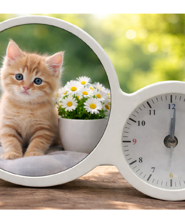 White clock with a round window showing a kitten and flowers on a wooden surface with a blurred green background